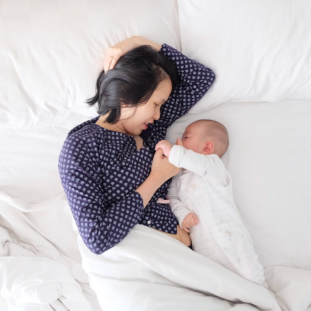 mother lying in bed with her newborn during the day