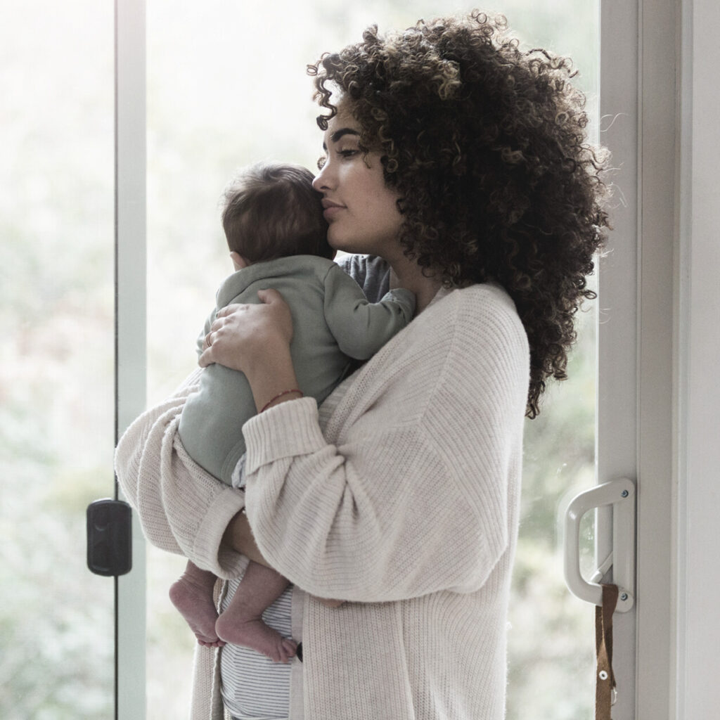 mother holding newborn and looking out window