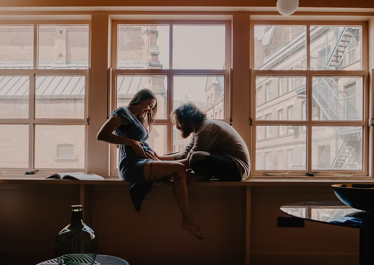 Photo of an expecting couple sitting in front of a window